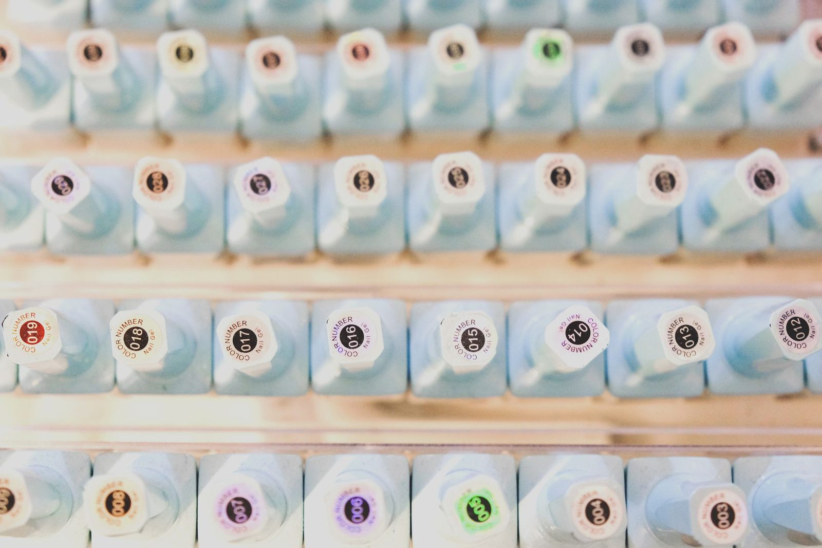 Fileiras de frascos de esmalte em gel numa prateleira em degraus de salão, tampas numeradas viradas pra frente — o arranjo que o organizador de esmalte impresso em 3D reproduz