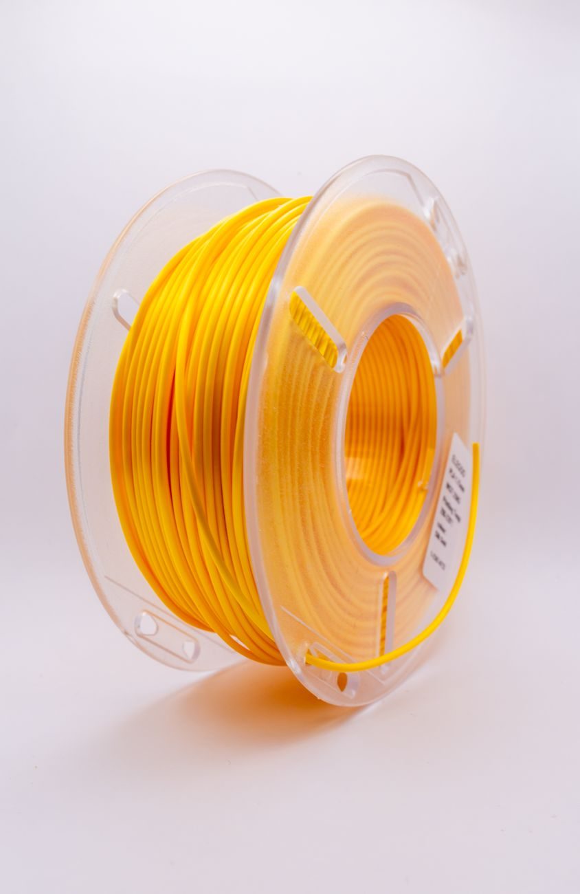 Rolo de filamento amarelo num carretel transparente sobre fundo branco