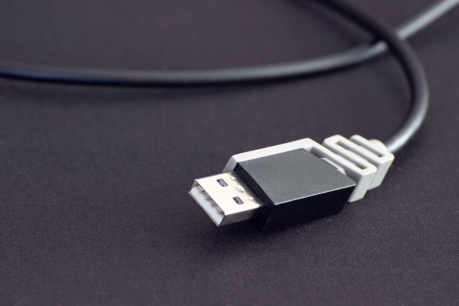 Cabo USB preto com o conector de metal em primeiro plano, sobre um fundo escuro