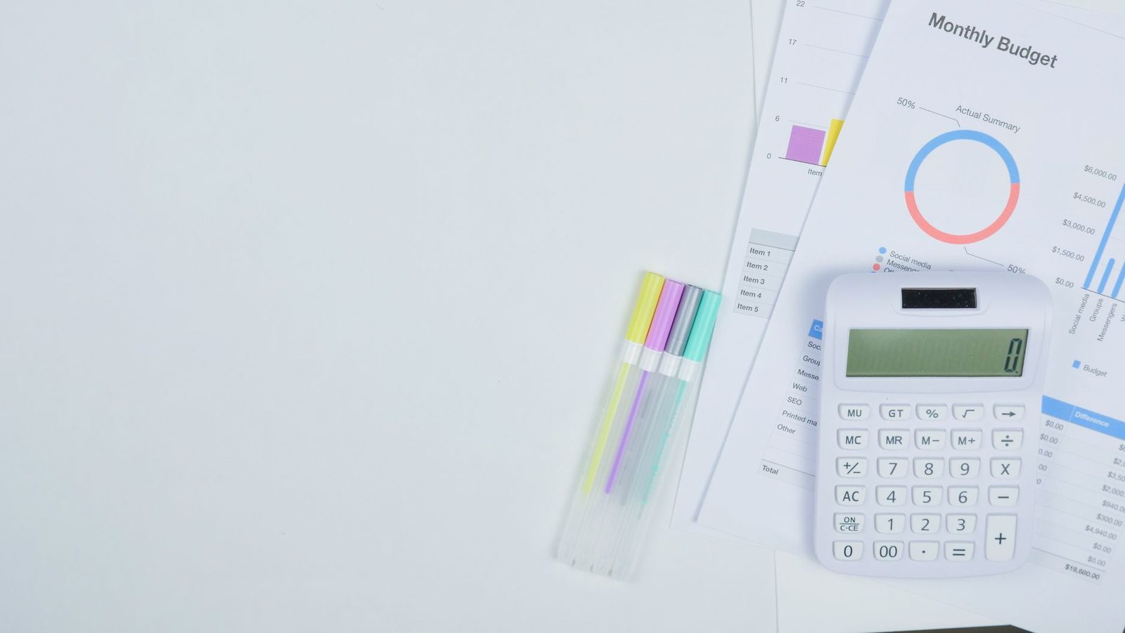 Calculadora branca sobre folhas de orçamento mensal com gráficos, ao lado de canetas marca-texto coloridas