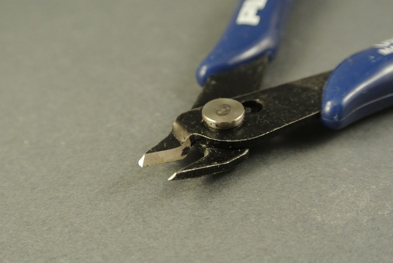 Alicate de corte rente pequeno, de cabo azul, com as lâminas em close sobre uma superfície cinza