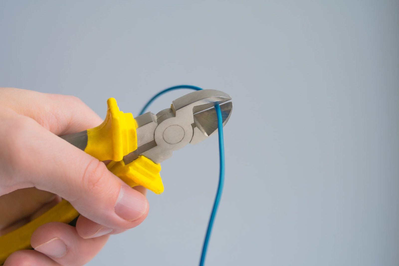 Mão segurando um alicate de corte diagonal de cabo amarelo, com um fio azul entre as lâminas