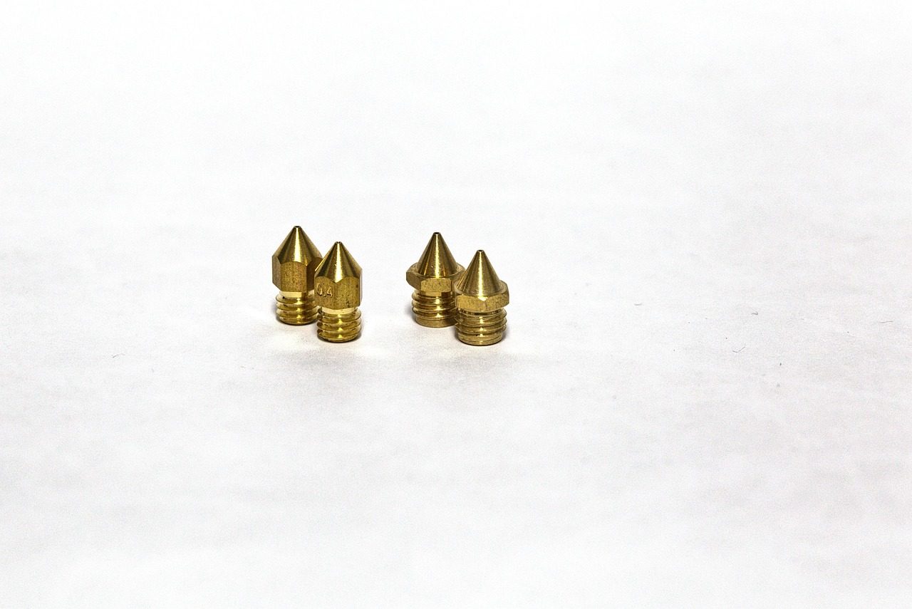 Quatro bicos de latão de impressora 3D, soltos sobre uma superfície branca