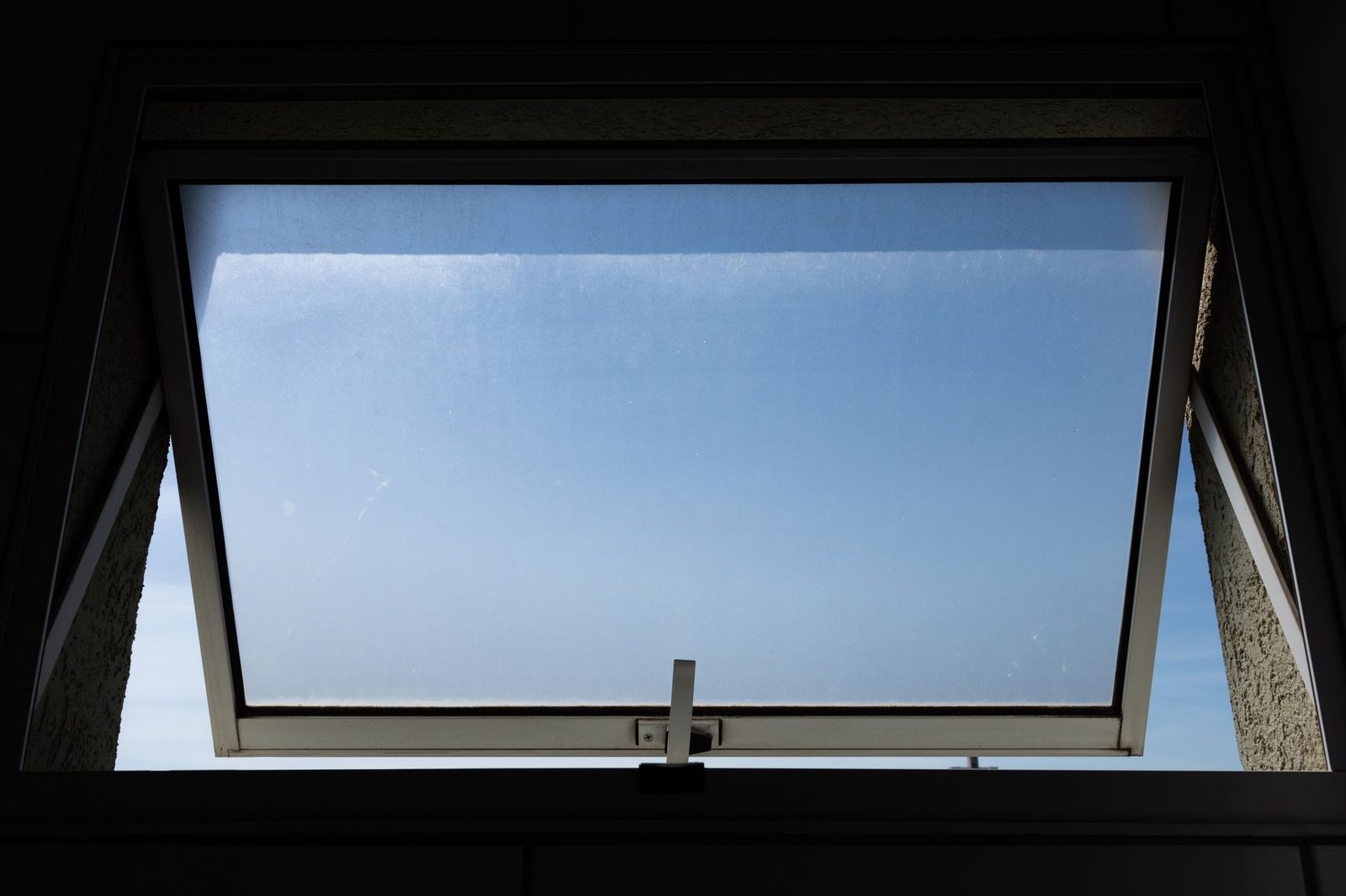 Janela basculante aberta vista de dentro do cômodo, com o céu azul do lado de fora