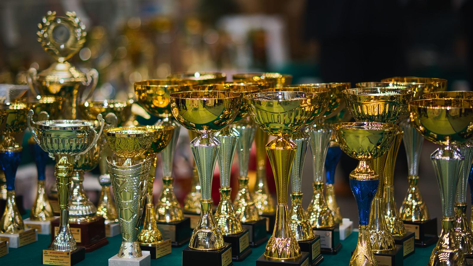 Fileira de troféus dourados, alguns com detalhes azuis, sobre uma mesa de exposição