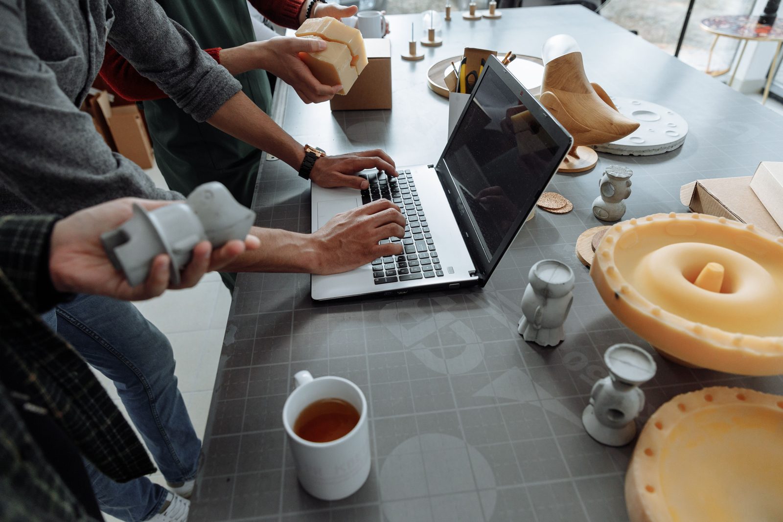 Moldes de silicone amarelados, pequenas peças cinza moldadas e um notebook sobre uma mesa de oficina