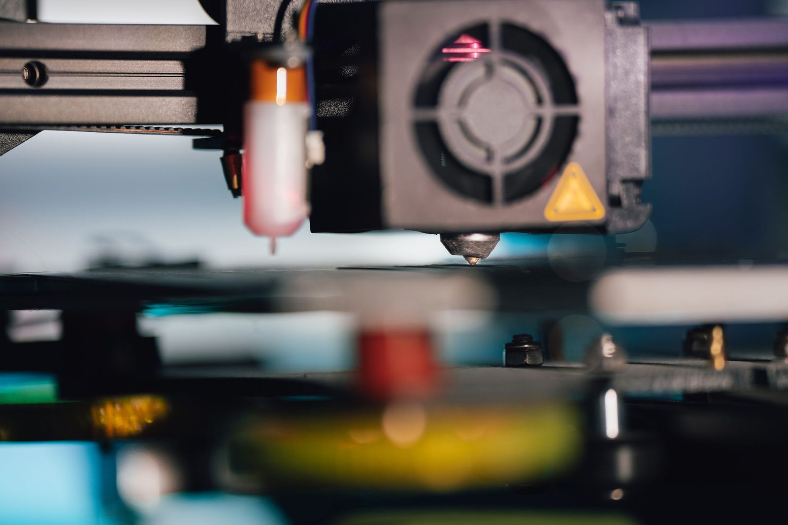 Cabeça de impressão de uma impressora 3D em close, com a ventoinha e o bico logo acima da mesa