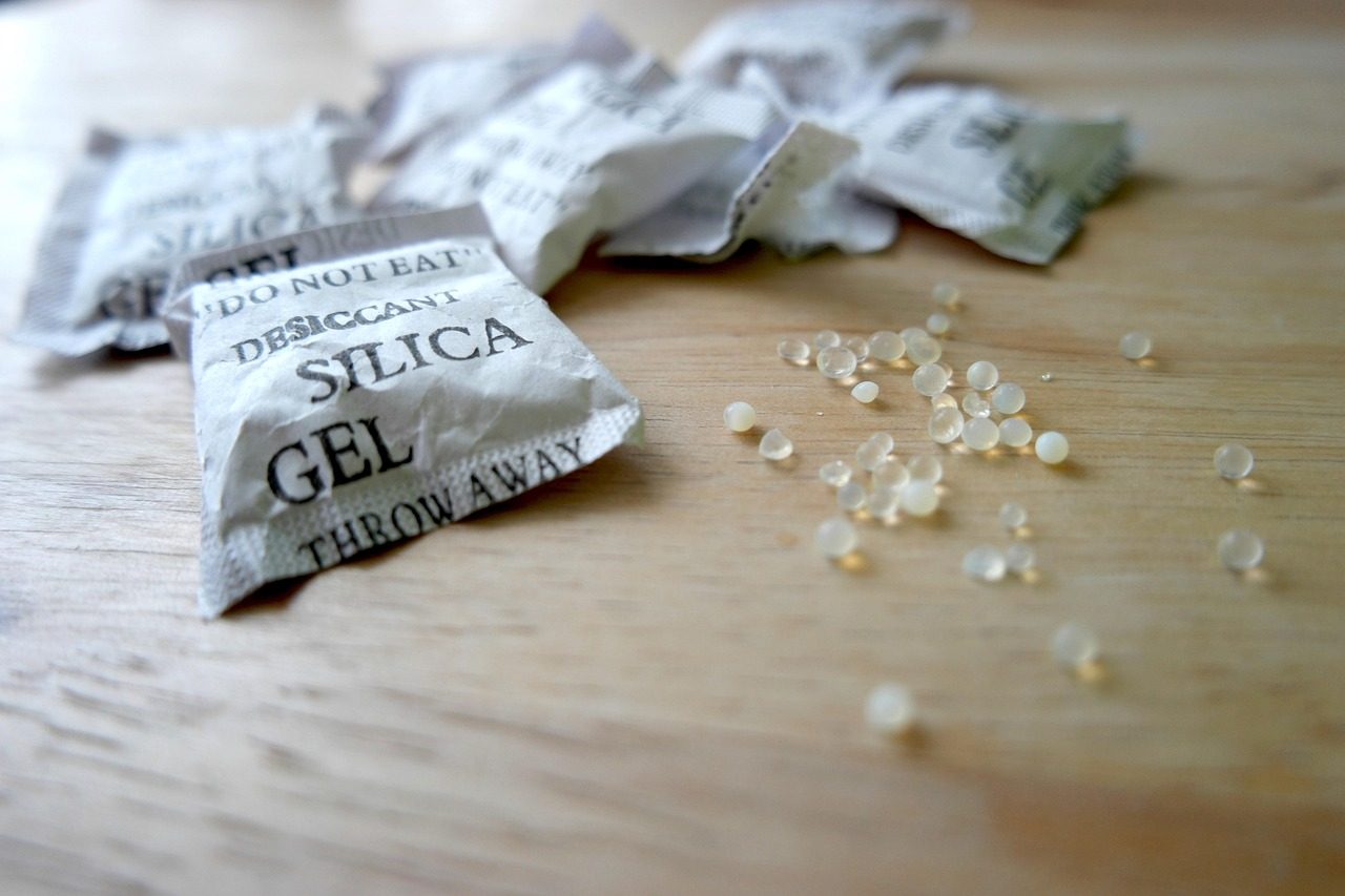 Sachês de sílica gel, o dessecante que absorve umidade, com as bolinhas espalhadas sobre uma mesa de madeira