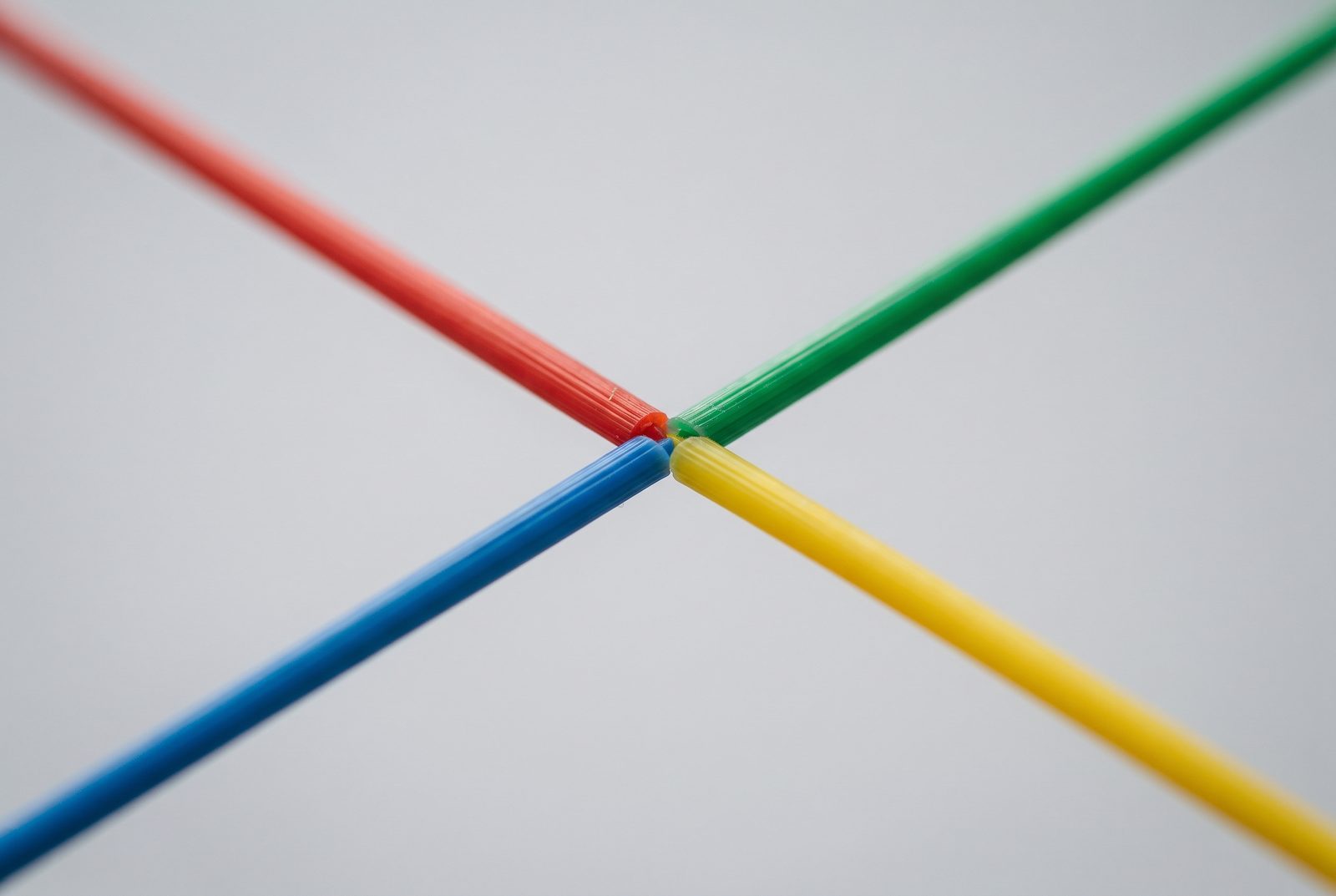 Quatro fios de filamento coloridos convergindo para um ponto sobre fundo neutro desfocado