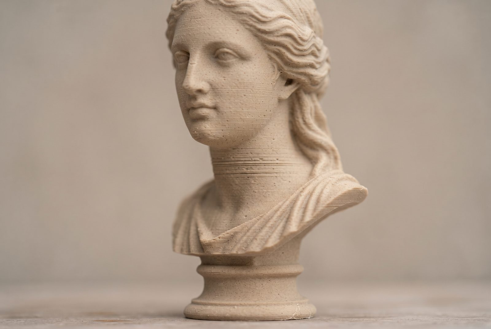 Busto impresso em 3D em PLA cor areia com linhas de camada visíveis sobre fundo neutro