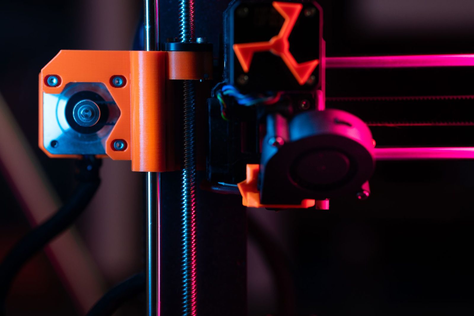 Fuso rosqueado vertical do eixo Z de uma impressora 3D, ao lado de uma barra lisa e do suporte laranja do motor, com a cabeça de impressão à direita