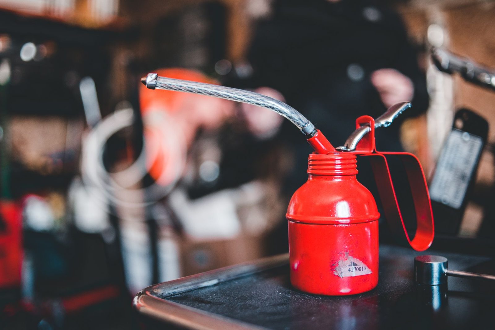 Frasco vermelho de metal com bico longo e flexível e alavanca de bombear, sobre uma bancada de oficina