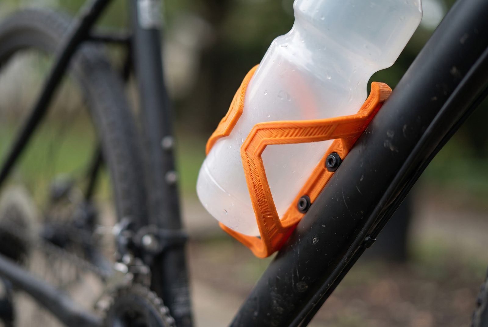 Suporte de garrafa impresso em 3D em PETG laranja fixado no quadro de uma bicicleta segurando uma garrafa lisa sem rótulo