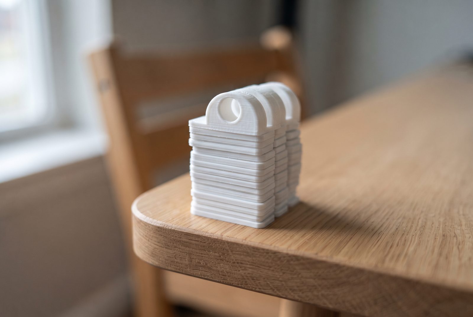 Clipes organizadores de cabo impressos em 3D em PLA branco empilhados na borda de uma mesa de madeira lisa