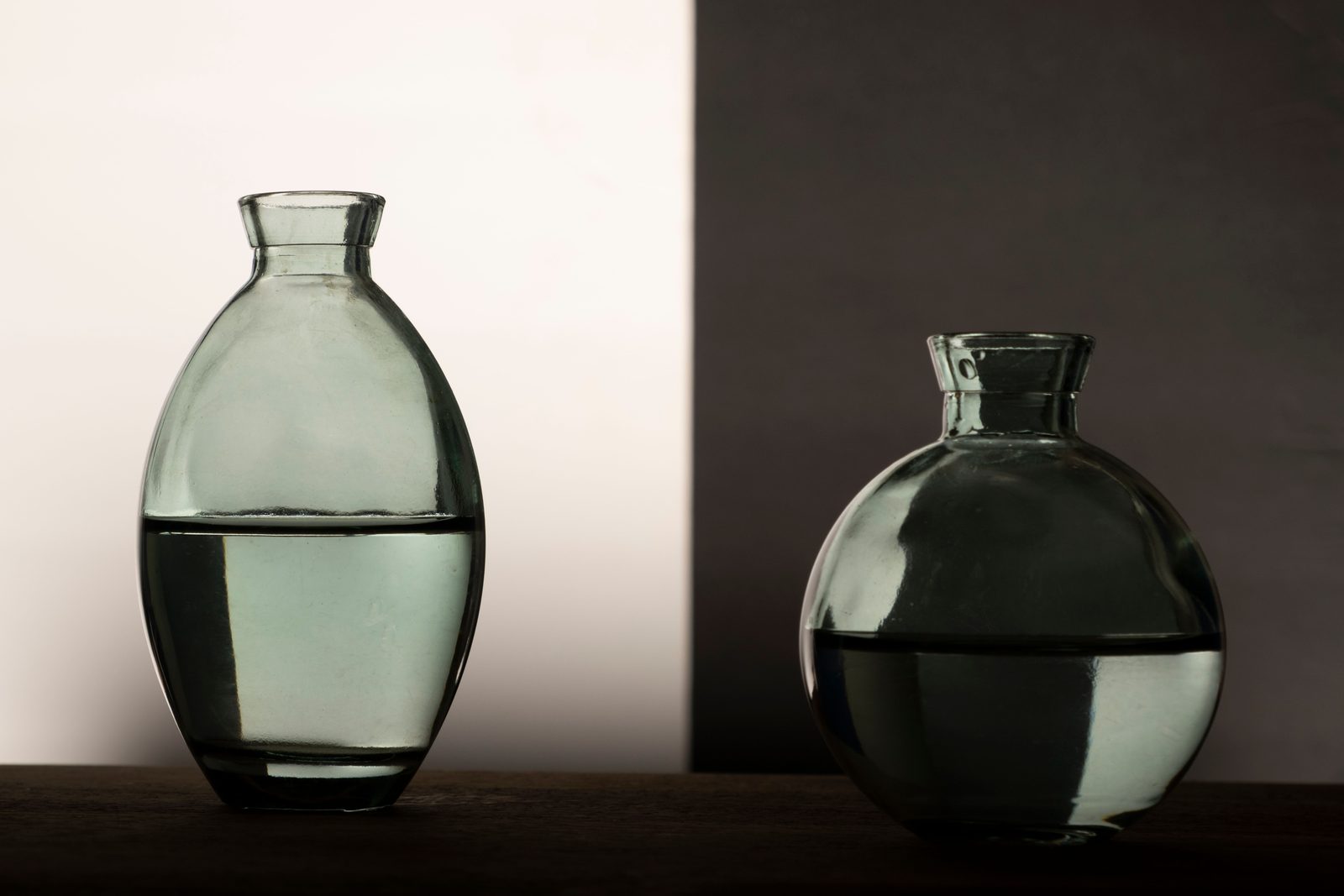 Dois vasos de vidro transparente com água sobre uma mesa escura