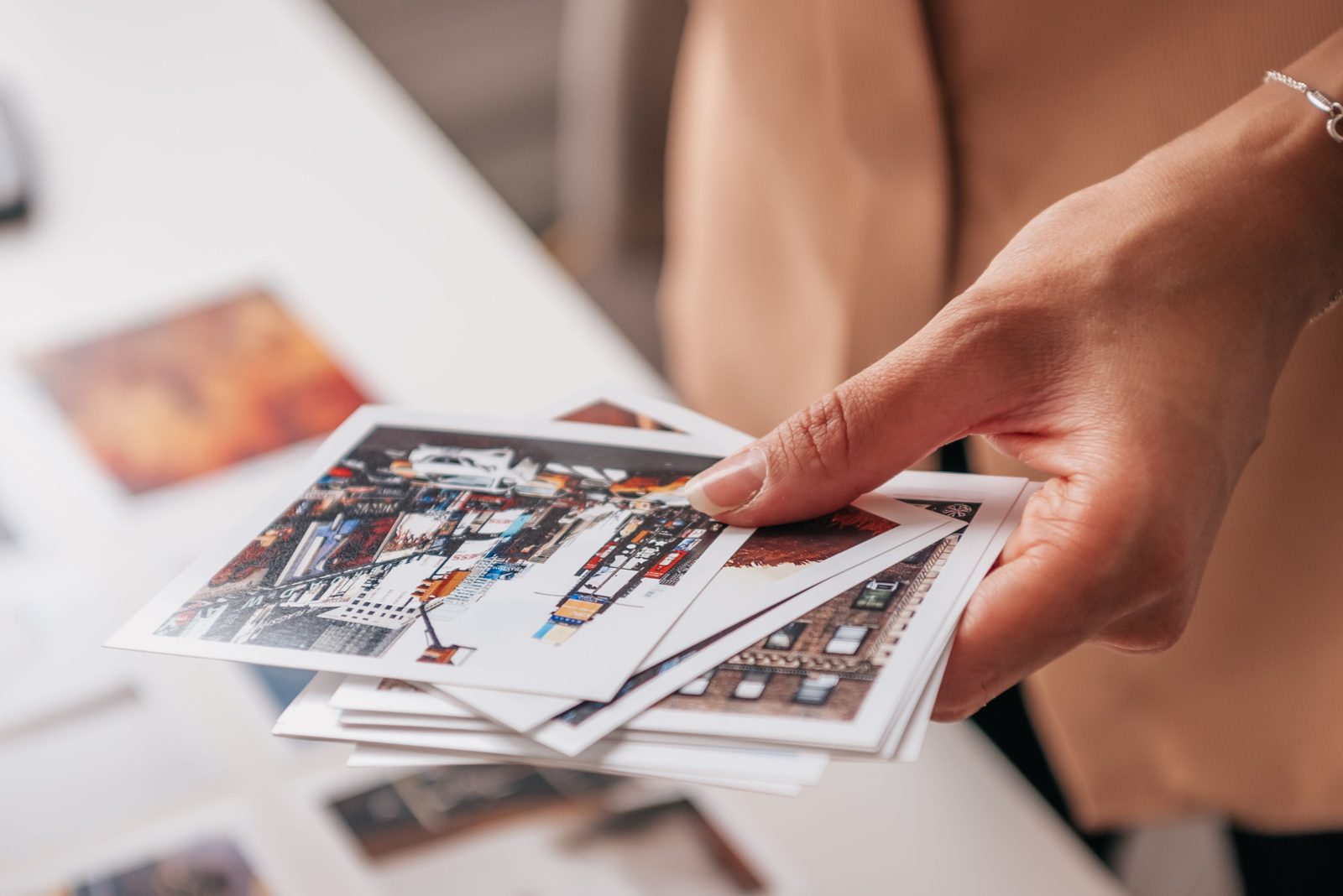 Mão segurando um maço de fotos impressas em papel, com cenas de rua coloridas, sobre uma mesa branca