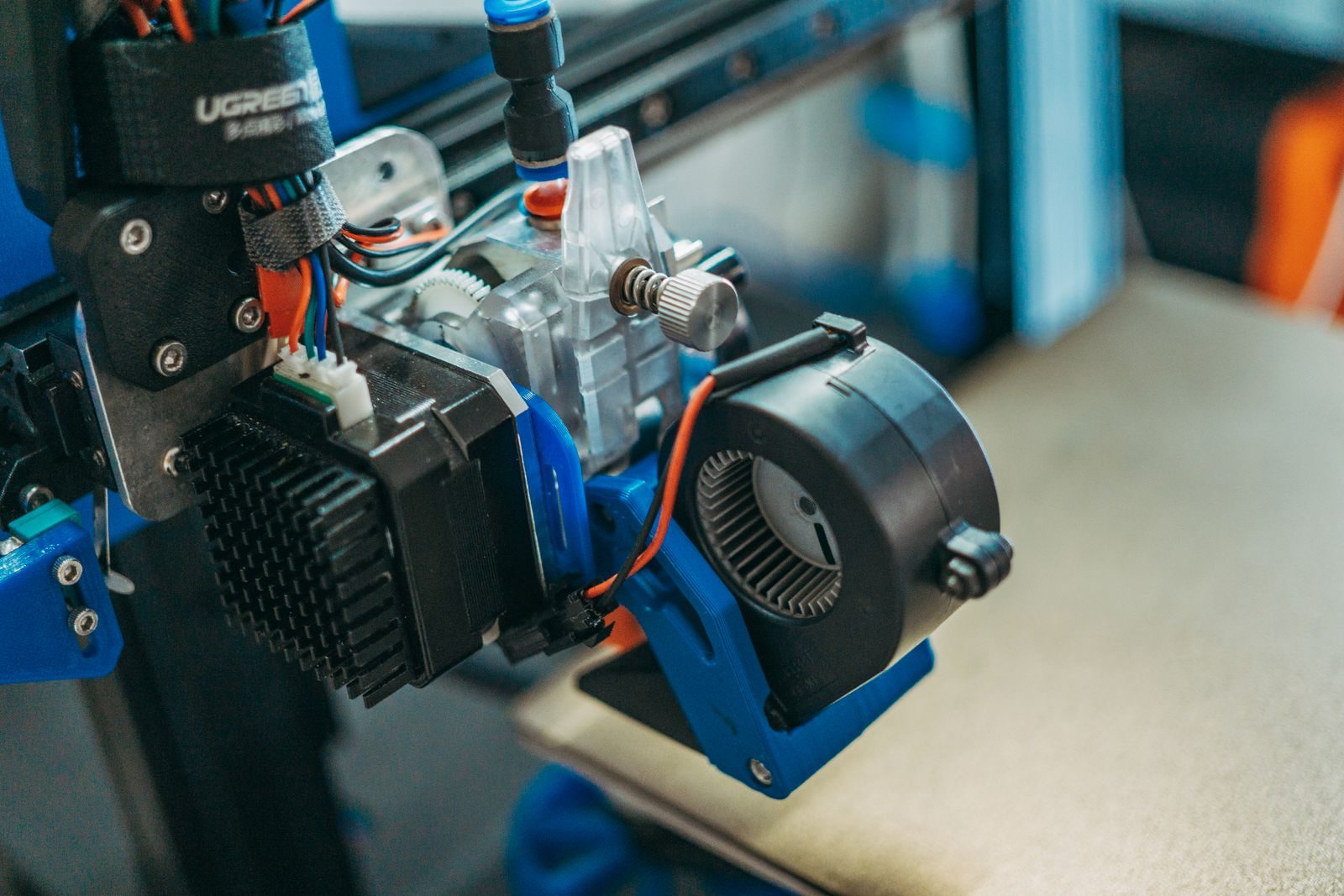 Cabeça de impressão 3D com ventoinha radial presa num suporte azul de plástico e cabos amarrados